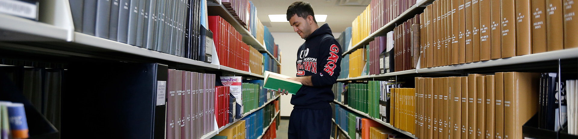 male UHD student reads a book in the aisle of the W.I. Dykes library