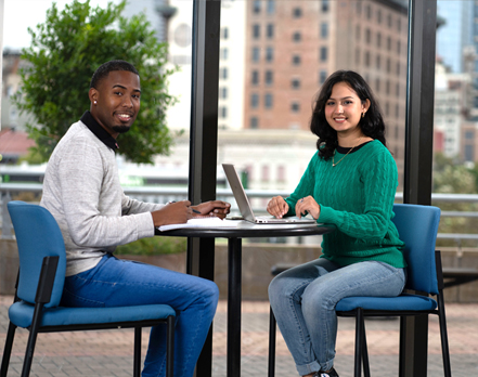 two UHD students at a table in the lounge area of the academic building