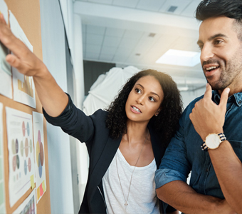 woman points to charts on a cork board while an man looks on
